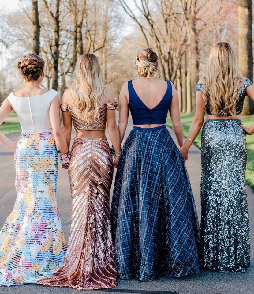 The back of four girls holding hands, wearing prom dresses.