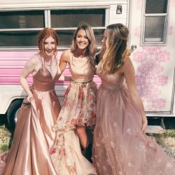 Three girls wearing blush pink homecoming dresses, smiling and laughing.