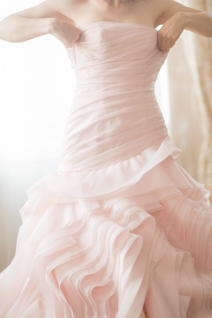 Woman putting on blush-pink mermaid-fitting formal dress with billowing ruffles. | Normans Bridal