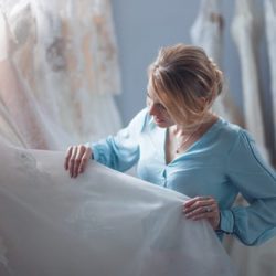 Girl in blue blouse examining a wedding dress in a bridal salon.