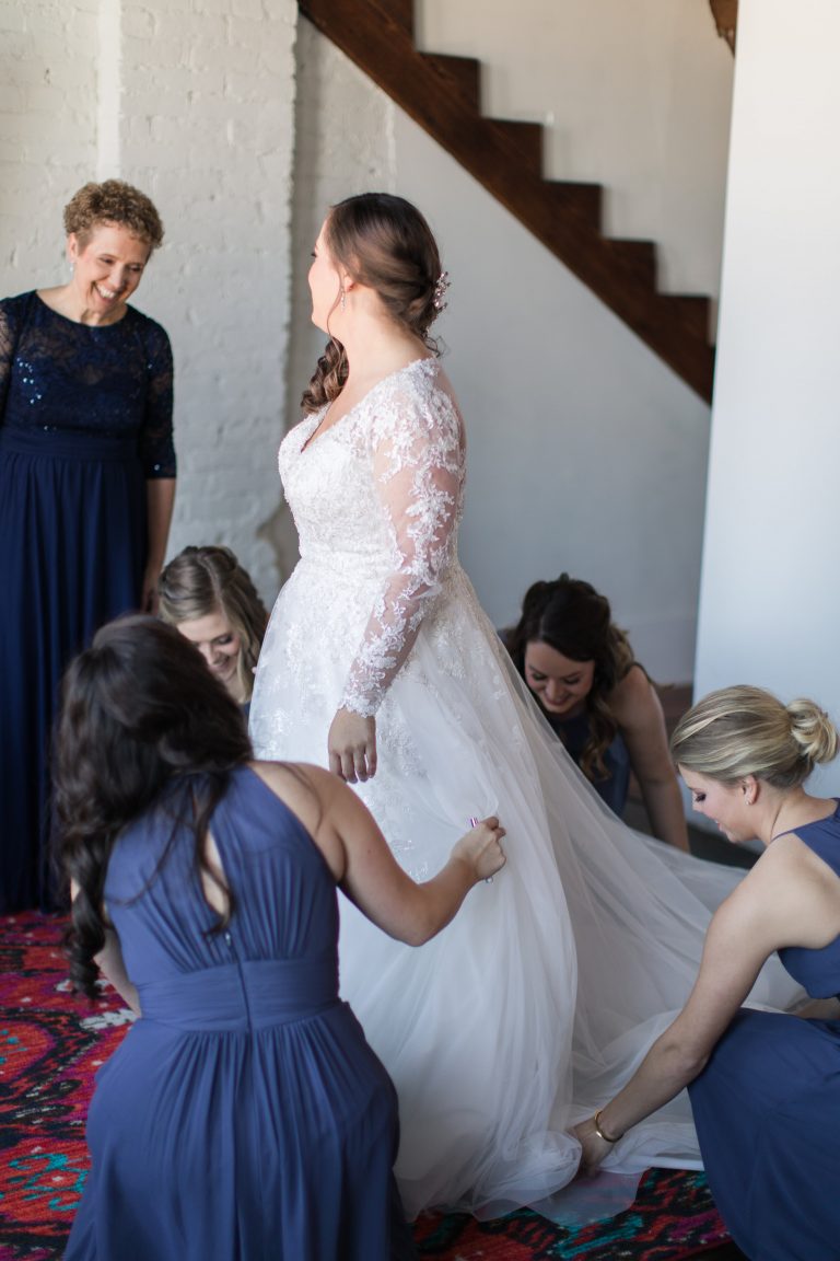 A Norman's bride getting help from her bridesmaids laying out her train.