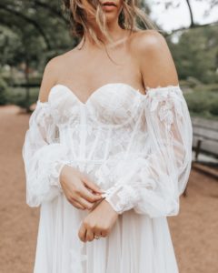 Bride wearing a sophisticated wedding gown, showcasing a unique sleeve style in a serene outdoor setting. | Normans Bridal